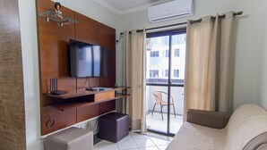 Ett modernt hotellrum med en platt-TV, träpanel, en soffa, en balkong med en stol och en skjutdörr i glas.