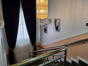 A staircase with a metal handrail, a chandelier, and two framed pictures on the wall.
