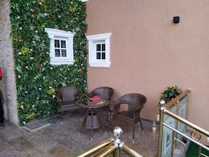 An outdoor seating area with wicker chairs and a table, a wall with a vertical garden, and a small window.