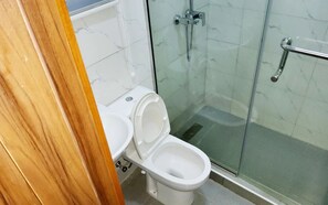 Ein Badezimmer mit Toilette, Waschbecken, Dusche mit Glastür und Handlauf.