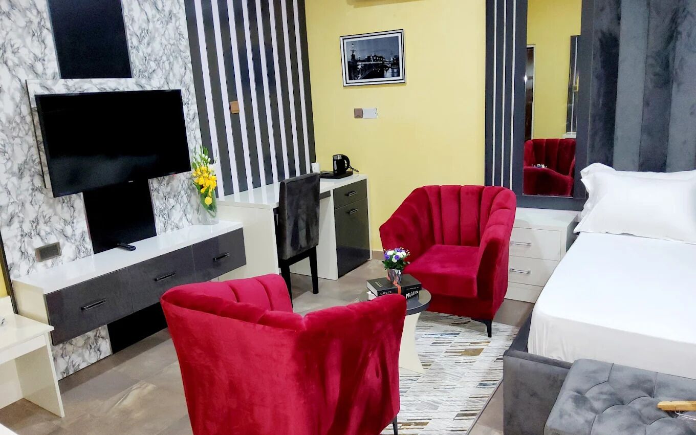 Ein Hotelzimmer mit einem Bett, zwei roten Sessel, einem Fernseher, einem Schreibtisch und einem Spiegel.
