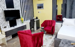 A hotel room with a bed, two red armchairs, a TV, a desk, and a mirror.