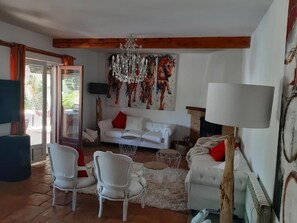 A living room with a white sofa, two white chairs, a chandelier, a painting of horses, and a large window.