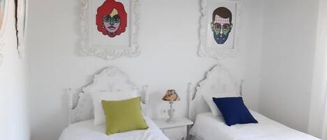 A bedroom with two beds, white bedding, and decorative wall art.