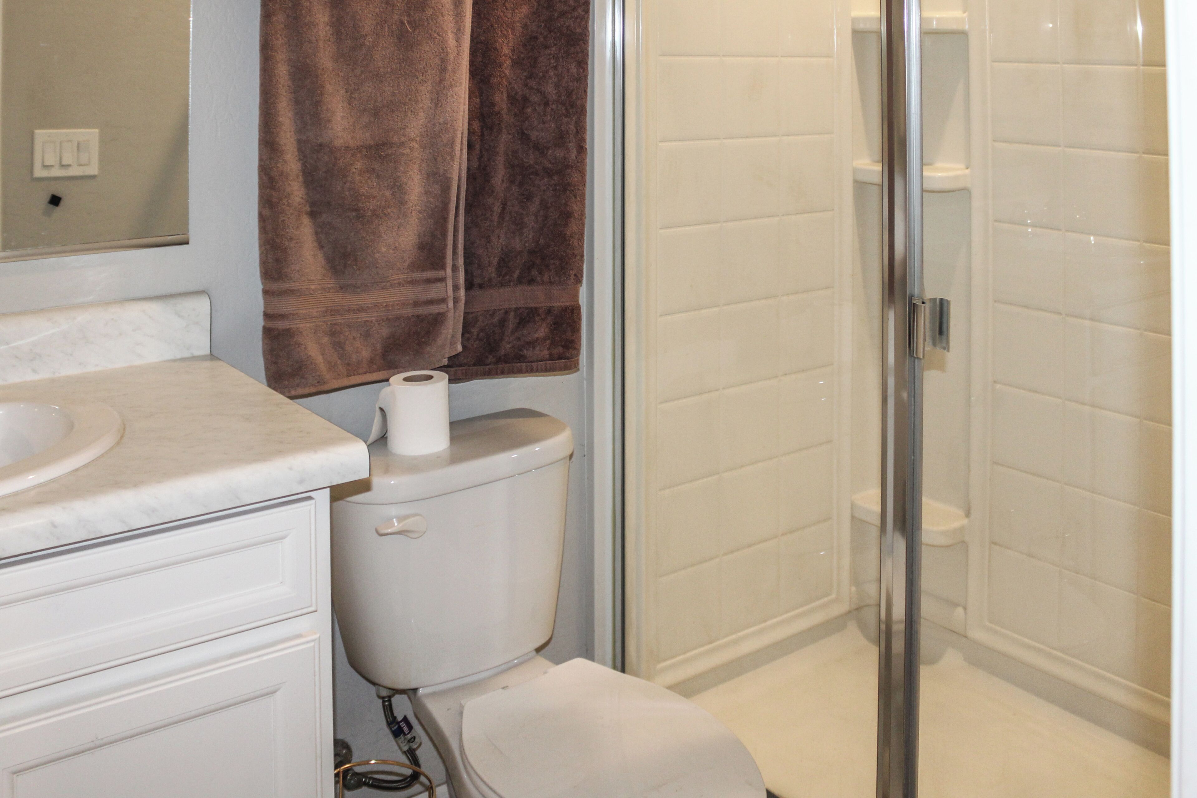 A bathroom with a toilet, a sink, a shower, and a towel hanging on the wall.