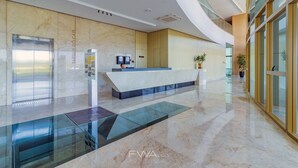 En moderne lobby med receptionsdisk, glas elevator og marmorgulv.