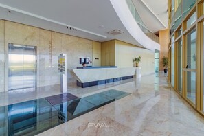Eine moderne Lobby mit einer Rezeption, einem gläsernen Aufzug und einem Marmorboden.