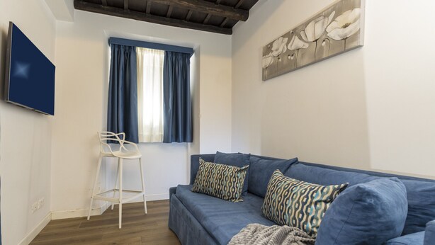 Een woonkamer met een blauwe bank, decoratieve kussens, een witte stoel en een schilderij aan de muur.