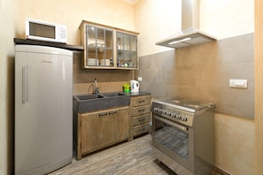 A compact kitchen with a refrigerator, microwave, wooden cabinets, a sink, and a stove. - San Francesco Ripa 2 - Fornarina Oasis Cottage (Rome)