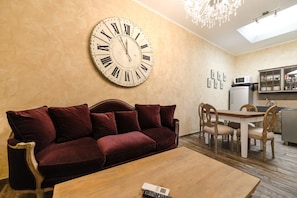 A living room with a large wall clock, a sofa, a wooden coffee table, and a dining area with chairs and a table. - San Francesco Ripa 2 - Fornarina Oasis Cottage (Rome)