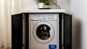 A compact washing machine with a control panel, a small potted plant, and a flat-screen TV mounted above it. - San Francesco Ripa 3 - Trilussa 3BR Group & Family Home (Rome)