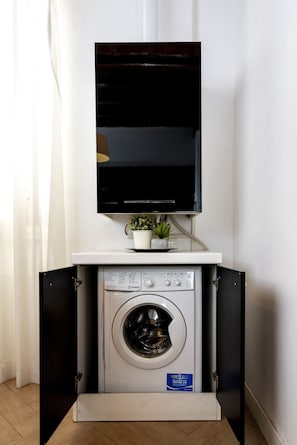 A compact washing machine with a control panel, a small potted plant, and a flat-screen TV mounted above it. - San Francesco Ripa 3 - Trilussa 3BR Group & Family Home (Rome)