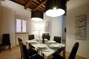 A dining room with a table set for six, a window with curtains, a lamp, and artwork on the walls. - San Francesco Ripa 3 - Trilussa 3BR Group & Family Home (Rome)