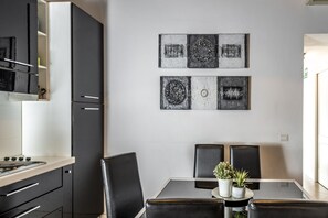 A modern kitchen with black cabinets, a stainless steel range hood, and a dining area with a glass table and black chairs. - San Francesco Ripa 3 - Trilussa 3BR Group & Family Home (Rome)
