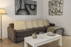 A living room with a brown sofa, white cushions, a white coffee table with decorative items, and wall art. - San Francesco Ripa 3 - Trilussa 3BR Group & Family Home (Rome)
