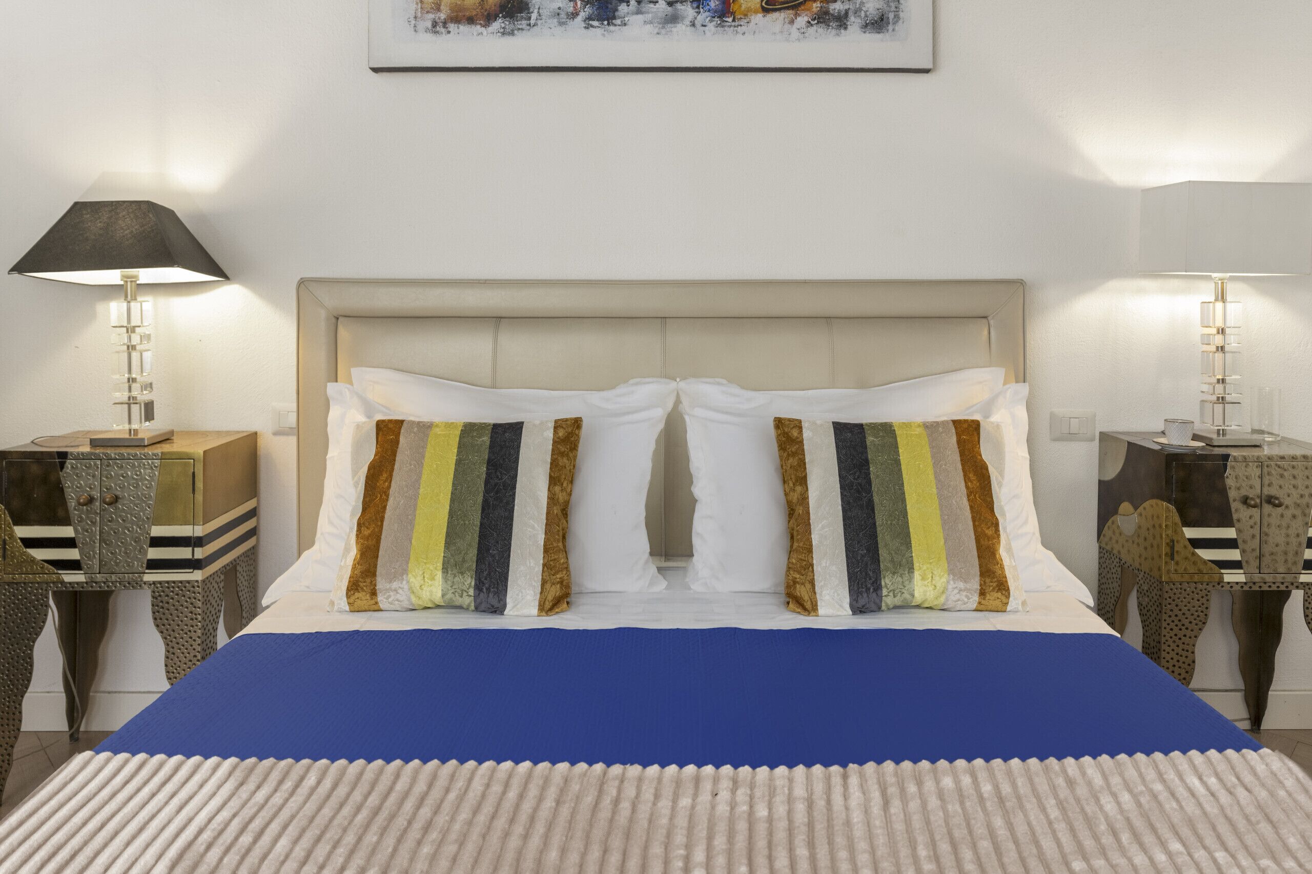 A hotel room with a bed, two bedside lamps, a nightstand, and a painting on the wall.