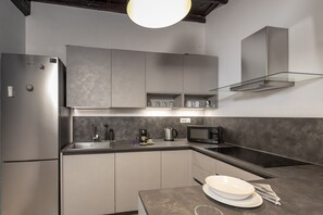 A modern kitchen with a built-in refrigerator, microwave, and a glass shelf unit. - San Francesco Ripa 4 - Lorenza 3BR Group & Family Home (Rome)