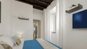 Ein Schlafzimmer mit Bett, einem an der Wand befestigten Fernseher und einem Flur zu weiteren Räumen.
