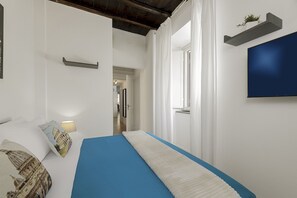 A bedroom with a bed, a TV mounted on the wall, and a hallway leading to other rooms. - San Francesco Ripa 4 - Lorenza 3BR Group & Family Home (Rome)