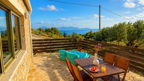Un patio de piedra con una mesa y sillas, vistas al mar y una valla de madera.