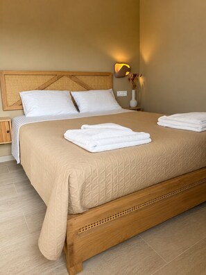 A neatly made bed with a beige quilt, two pillows, and two folded white towels on the bed.