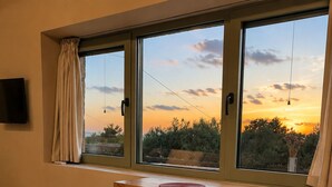 Una habitación con una mesa de madera y dos sillas, un televisor montado en la pared y un ventanal con vistas al atardecer.