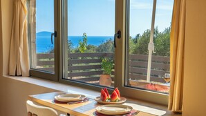 Una mesa de comedor con platos y cubiertos, una copa de vino y vistas al mar a través de amplios ventanales.