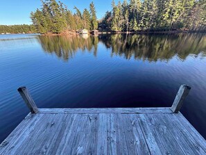 A wooden dock extending into calm water with a forested shoreline in the background. - Brantingham Lake cabin with waterfront access (Greig)