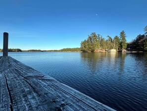Eine Holzstele führt ins ruhige Wasser, umgeben von Bäumen und einem klaren Himmel.
