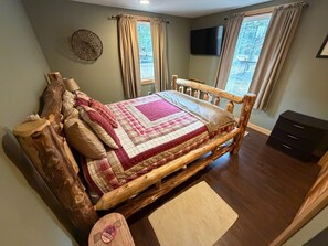 A bedroom with a wooden bed, a television, and a window with curtains. - Brantingham Lake cabin with waterfront access (Greig)