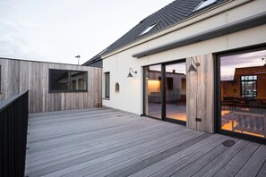 Ein modernes Gebäude mit einer Holzterrasse, großen Schiebeglastüren und einem einsehbaren Innenbereich mit Essbereich.