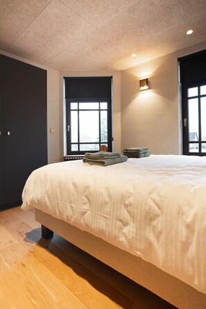 Ein Schlafzimmer mit einem großen Bett, einem Fenster mit Jalousien, einer Wandleuchte und einer Tür.