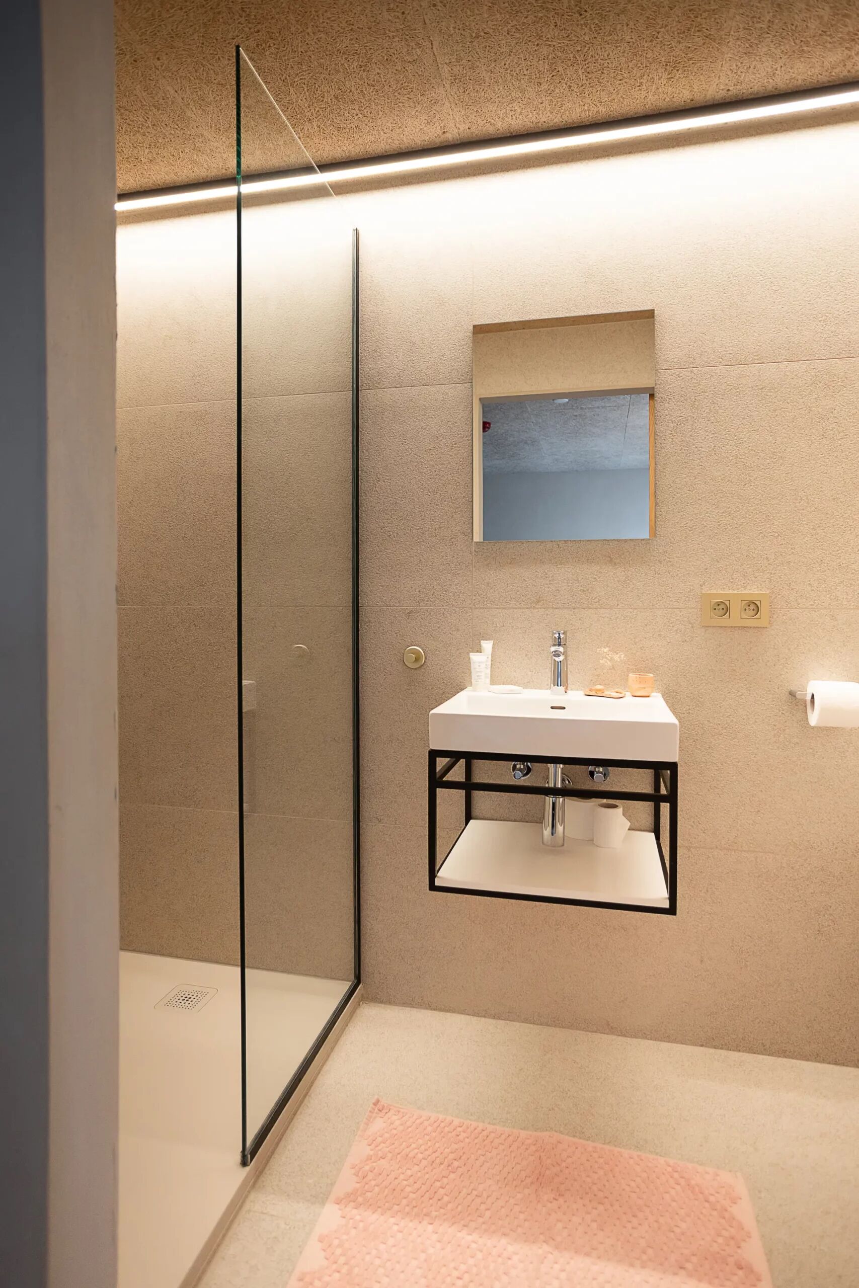A modern bathroom with a glass shower enclosure, a sink with a mirror above, and a towel on the floor.