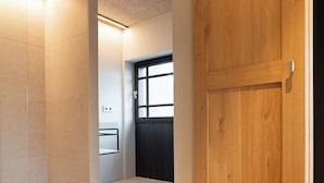 Un couloir avec une porte en bois, un mur recouvert de carreaux et une fenêtre avec des stores.