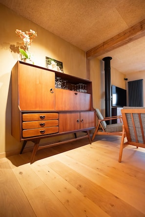 Ein Holzkabinet mit Schubladen, eine Blumenvase, ein Stuhl und ein Fernseher in einem Raum mit Holzboden.