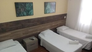 A hotel room with two single beds, a nightstand, a small table, and two wall-mounted paintings. - Hotel Natal de Santos  (Santos)