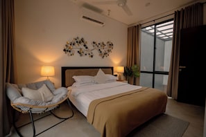 Habitación de hotel con cama, una silla, una obra de arte en la pared y una ventana con cortinas.