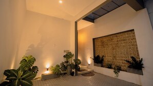 A modern interior with a tiled floor, potted plants, a wall-mounted light, and a textured wall.