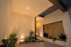 A modern interior with a tiled floor, potted plants, a wall-mounted light, and a textured wall. - LADY LAVINIA GUEST HOUSE (Mount Lavinia)