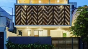 A modern two-story house with a flat roof, a wooden upper floor, and a patterned facade.