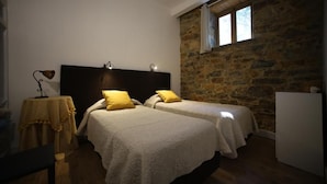 Quarto com duas camas, parede de pedra, janela e mesa com abajur.