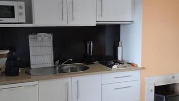 A compact kitchen with white cabinets, a microwave, a sink, and a stove.