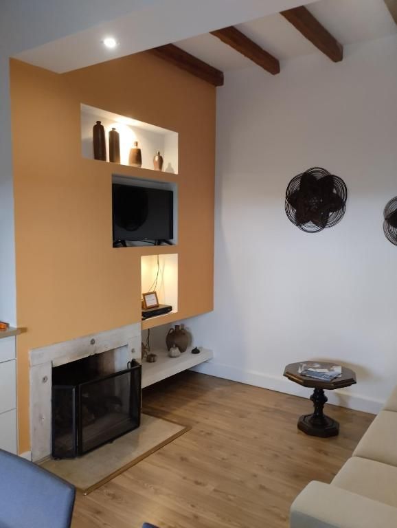 Una sala de estar con chimenea, televisor montado en la pared y una mesa redonda con un libro.