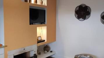 Una sala de estar con chimenea, televisor montado en la pared y una mesa redonda con un libro.