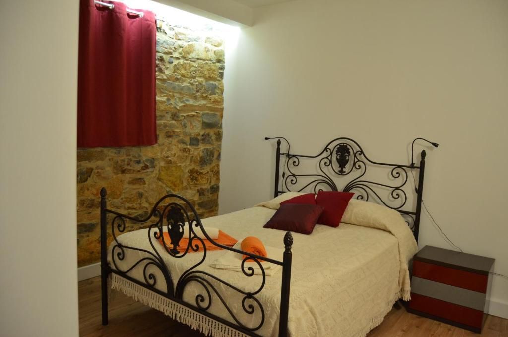 A bed with a metal frame, a stone wall, and a red curtain.