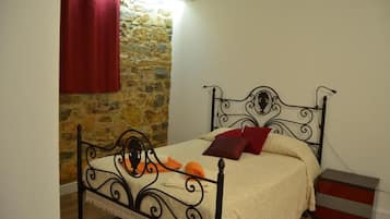 A bed with a metal frame, a stone wall, and a red curtain.