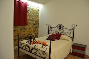 A bed with a metal frame, a stone wall, and a red curtain.