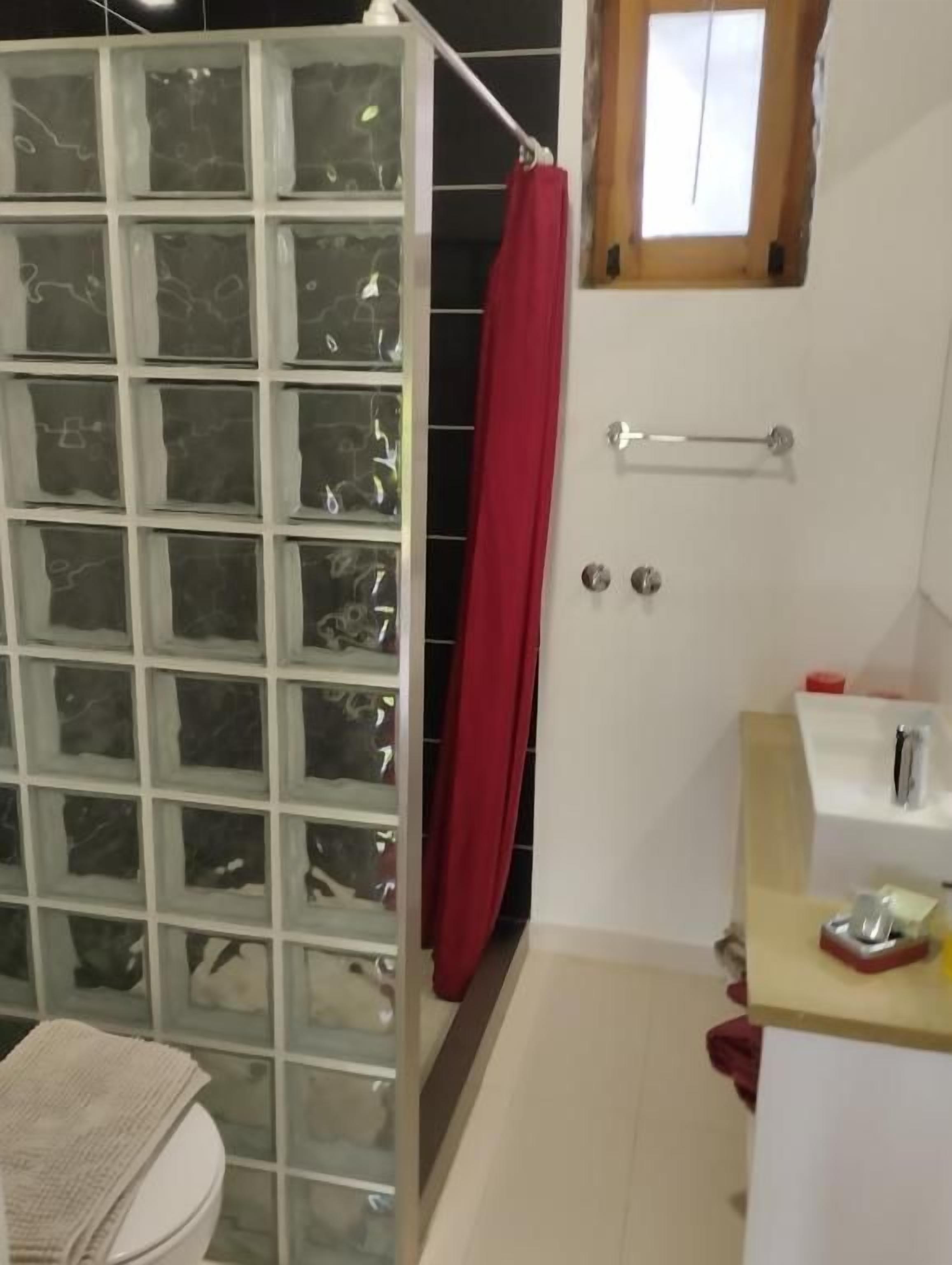 Et badeværelse med brusekabine i glas, toilet, vask og spejl.