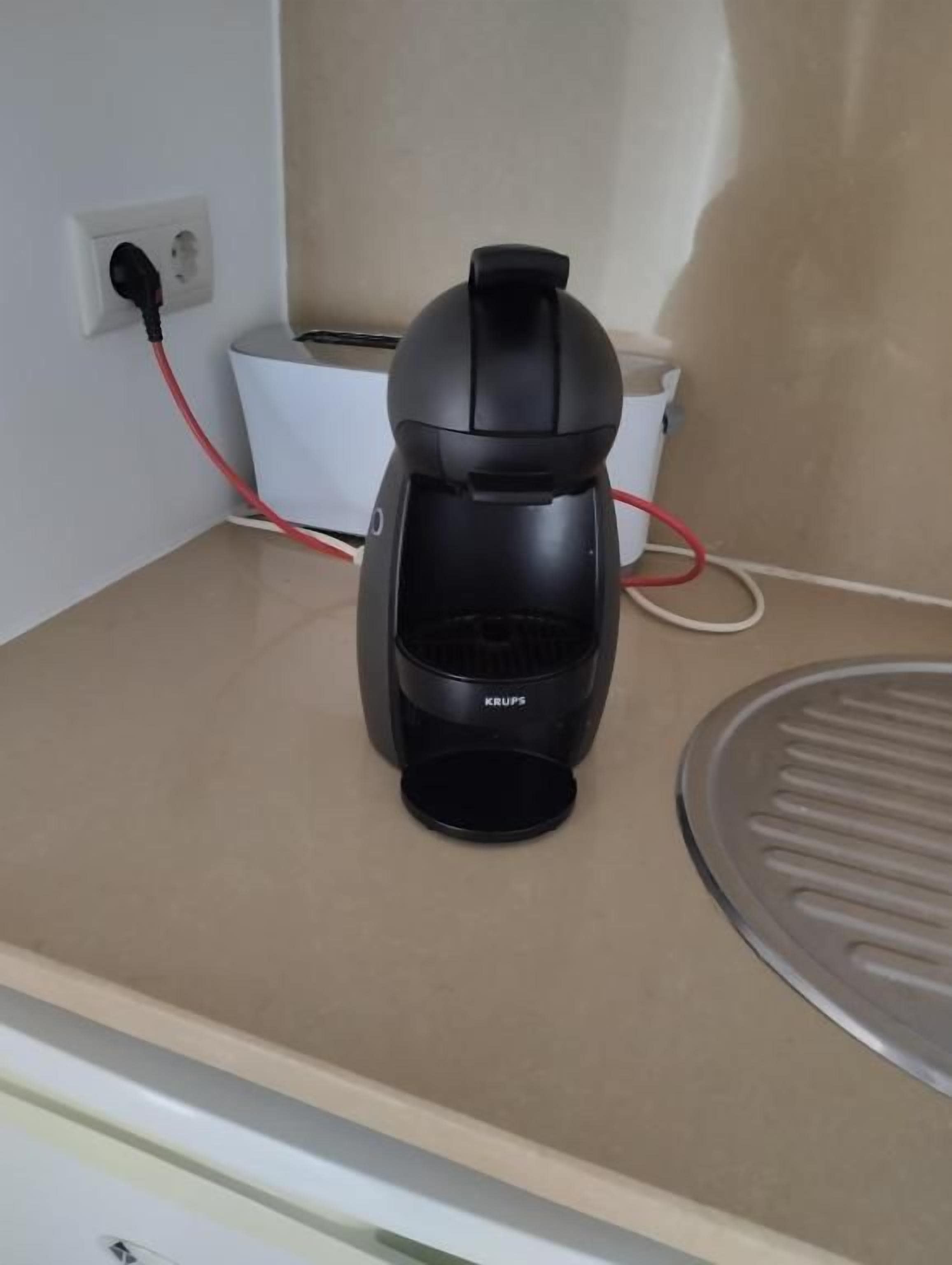 A coffee maker on a countertop with a power outlet and a white appliance in the background.