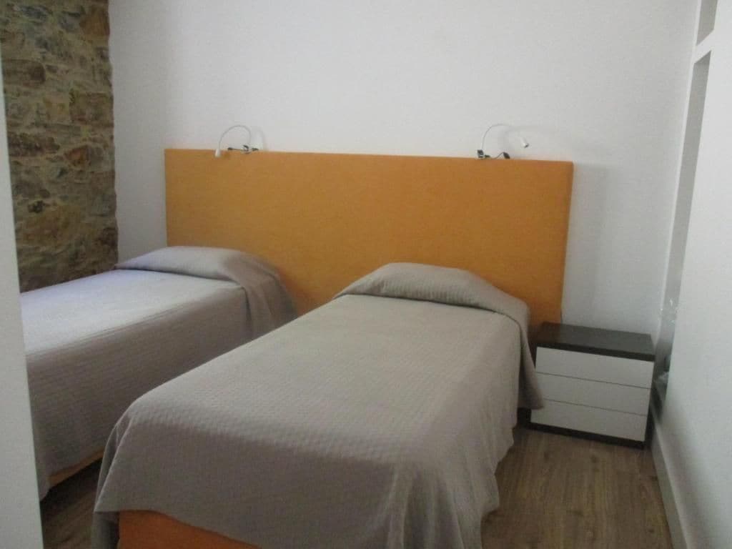 Una habitación con dos camas individuales, una mesita de noche y una pared de piedra.